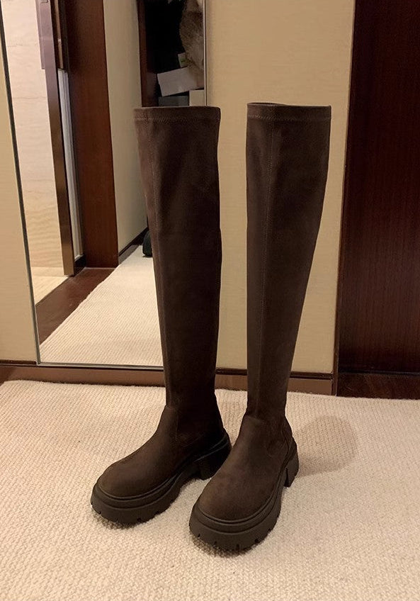 A pair of dark brown knee-high boots with chunky lug soles, shown standing on a beige carpet in front of a mirror and wooden door. Chinese text is printed below the photo.